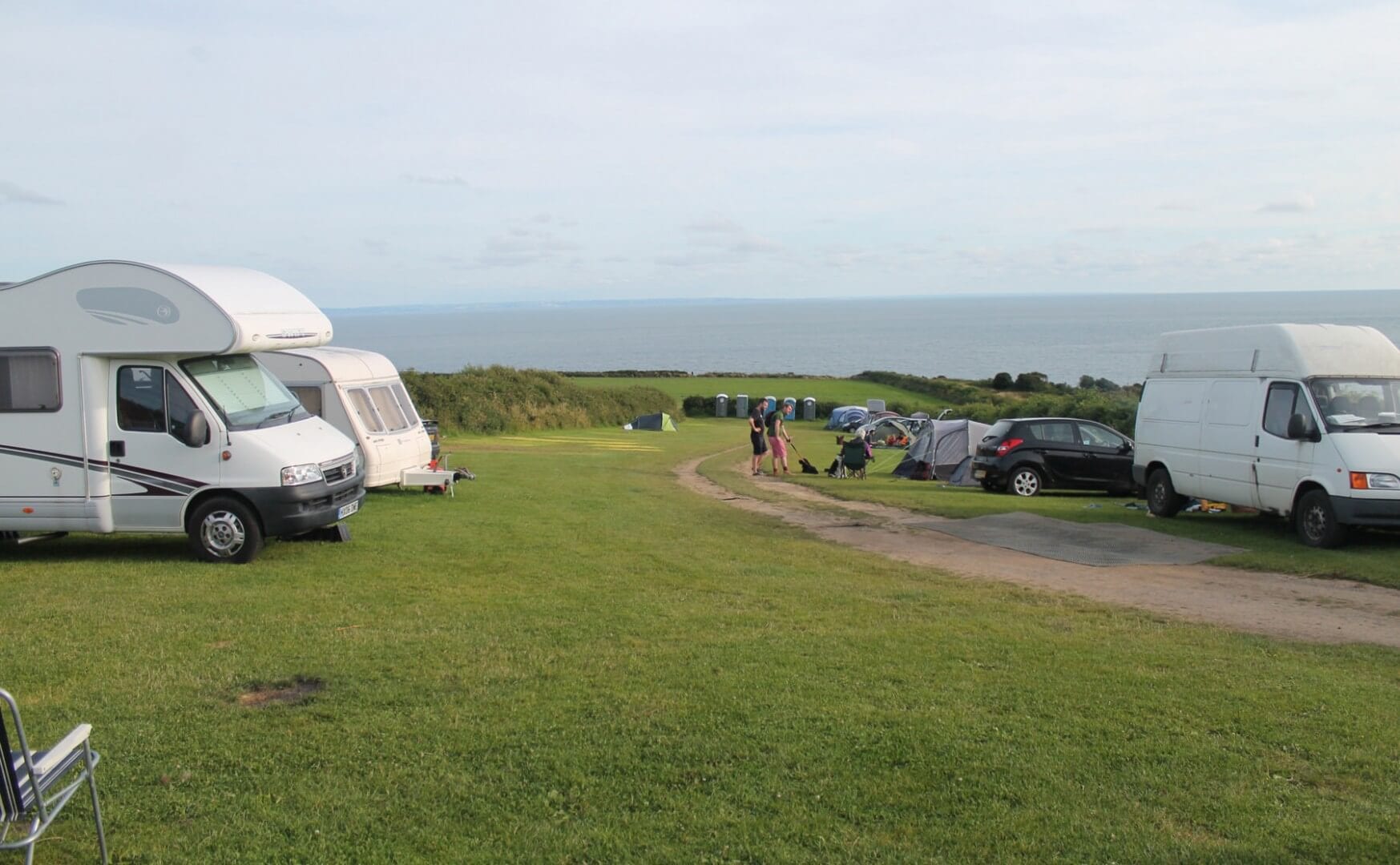 A picture of the camping facilities at Eastern Slade Barn. Pictured is a few tents, a few caravans and some grass. the sky is a bit grey.