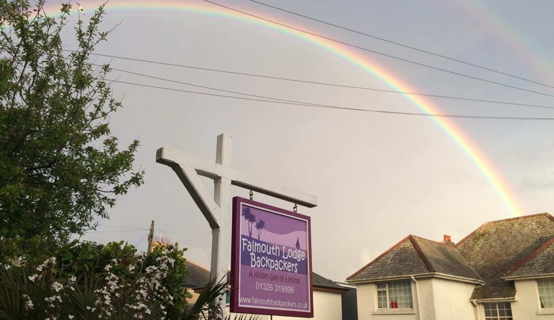 a pictures of the falmouth backpackers sign and behind the sign, in the sky is a rainbow. 