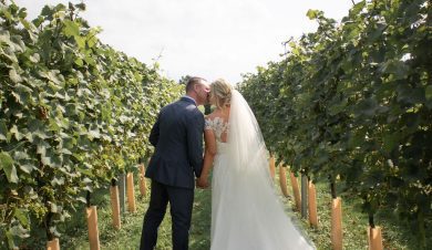 A man and a woman in a suit and wedding dress kiss each other in a vineyard