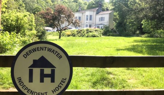 Derwentwater independent hostel sign attached to a fence with the hostel in the background