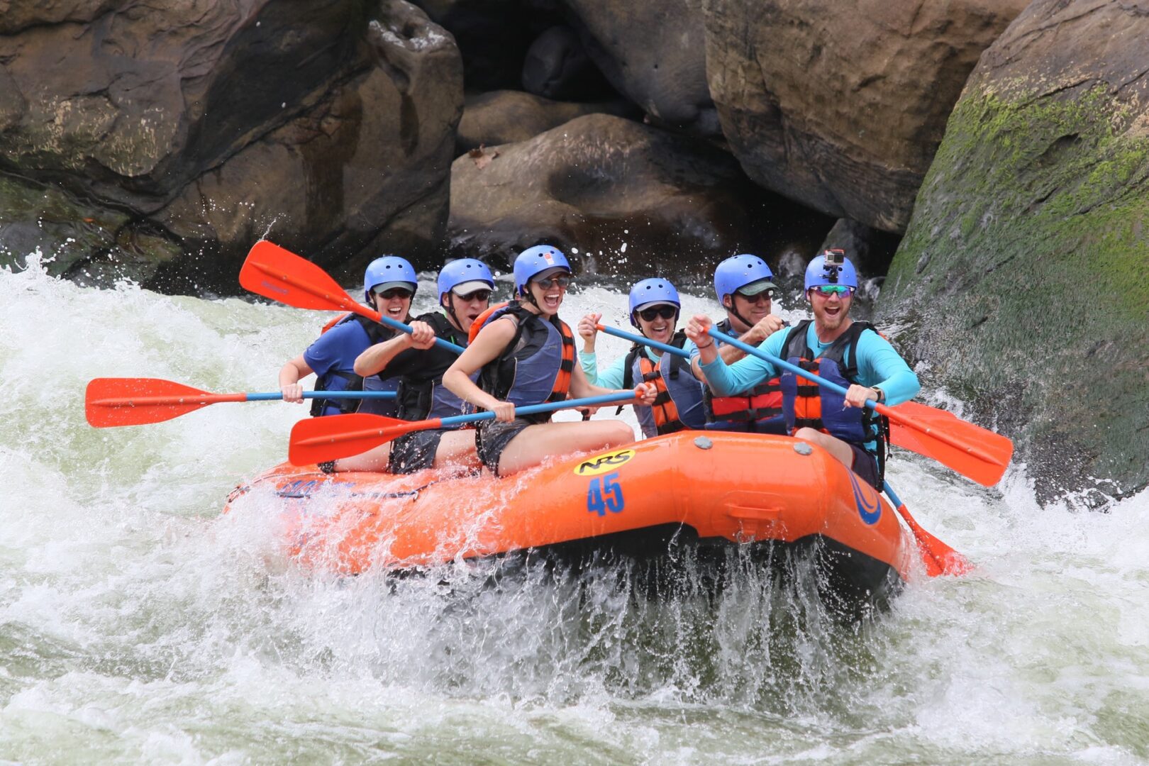 The picture depicts 6 men and women having a fun time navigating trechourous waters while white water rafting.