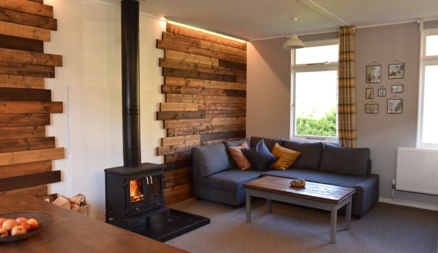 Modern lounge with grey corner sofa and modern wall panelling and blazing wood burner