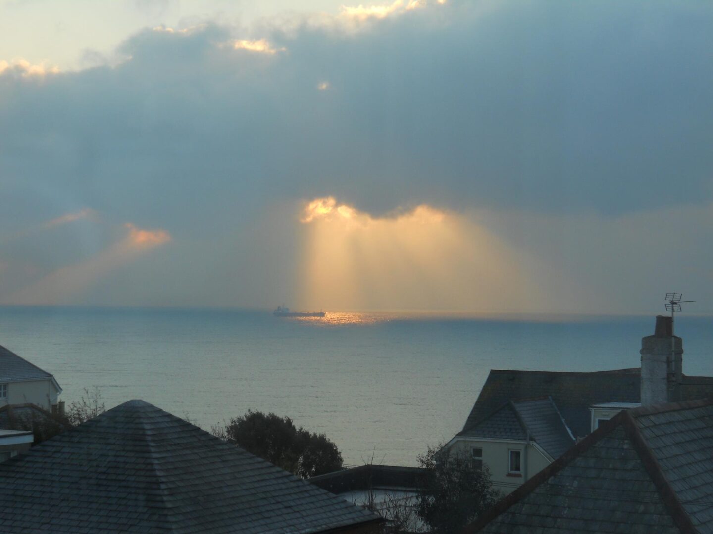 View over roof tops to the sea with sunlight shining through a gap in the clouds on a ship