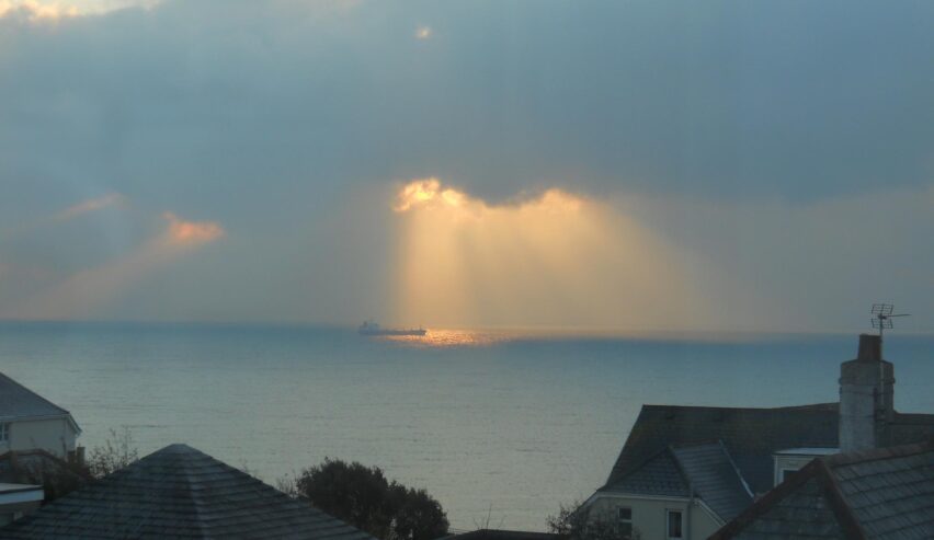 View over roof tops to the sea with sunlight shining through a gap in the clouds on a ship