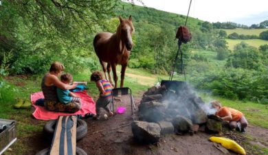 a woman with three children and a horse cooks on a campfire in the woods