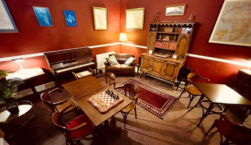 Cosy lounge with deep red walls, aand antique style dark wood furniture a piano and a chess board