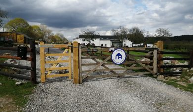 Gate with IHUK sign and white farmhouse down the drive
