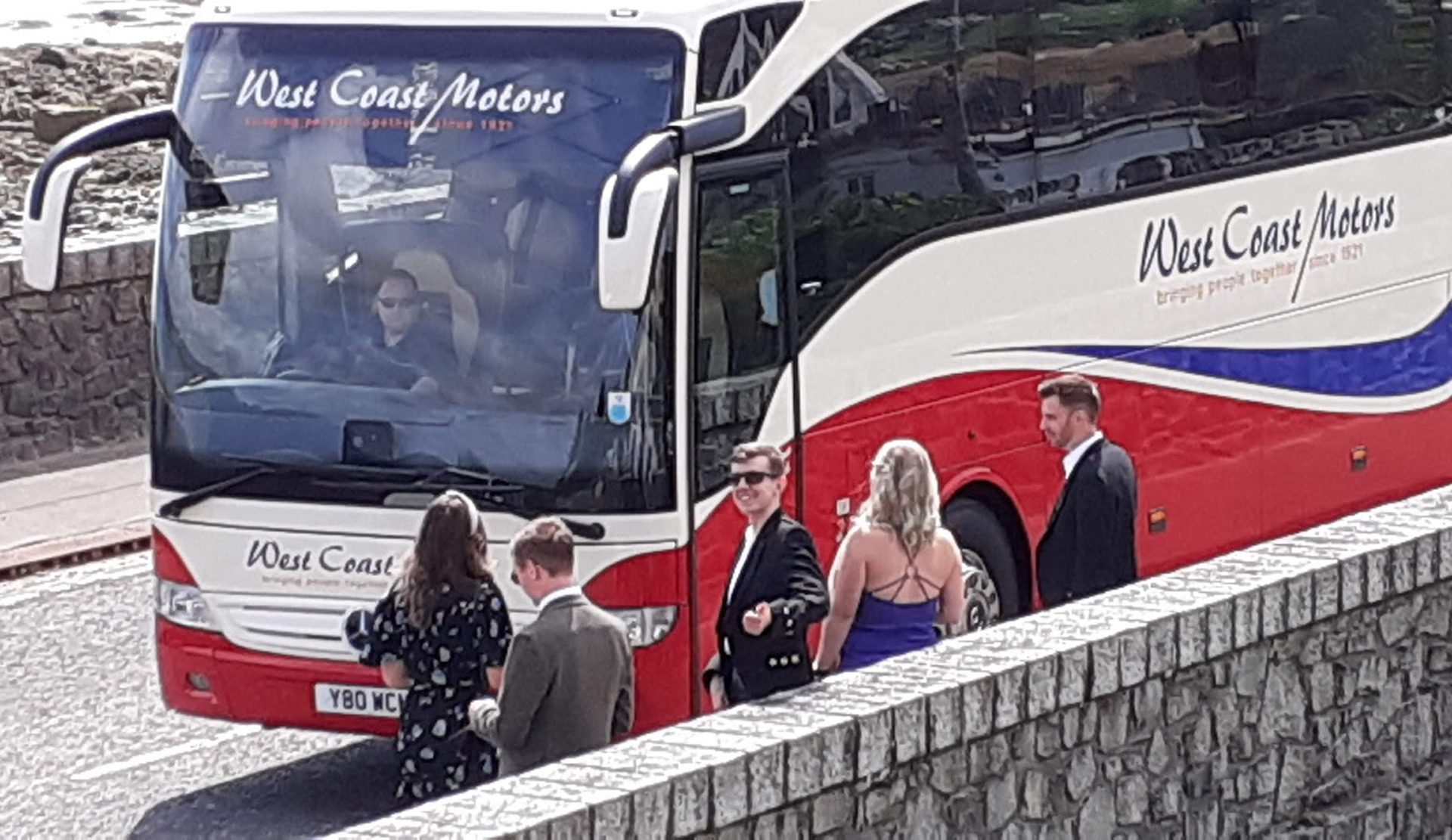 Wedding guests are about to board the coach that takes them to the wedding. They look happy and ready for the day