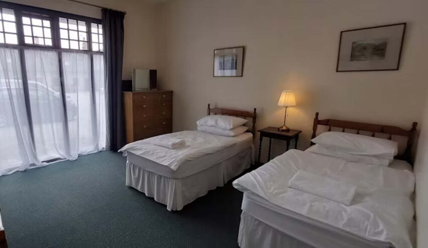 twin bed room at Mar Lodge Bunkhouse with large window and view of carpark